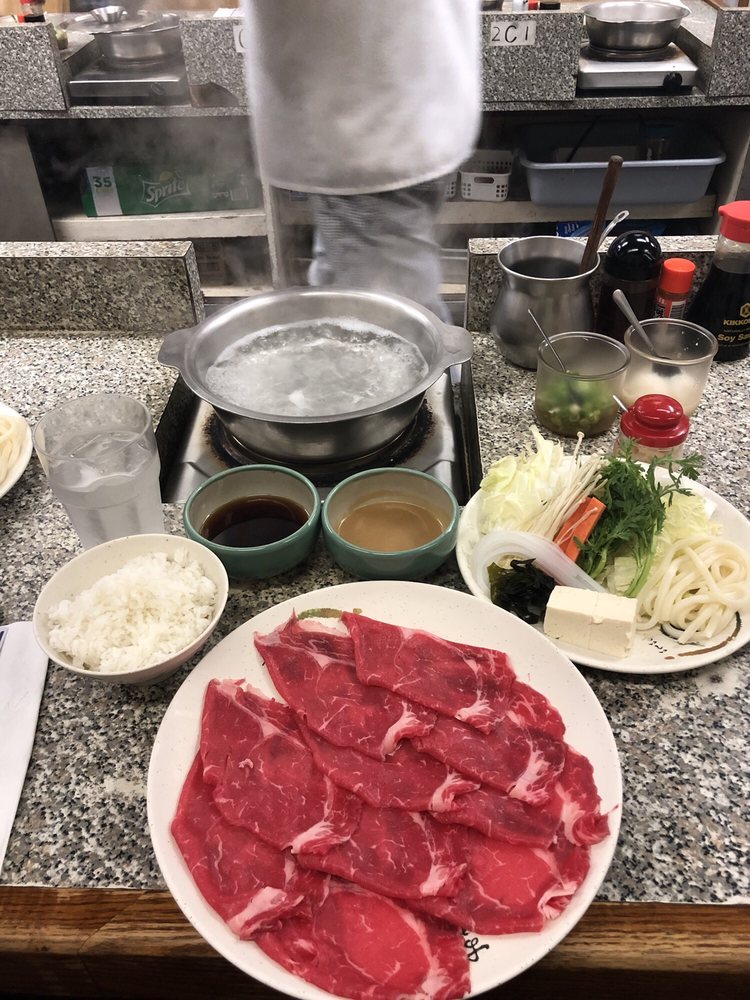 Thin-sliced raw beef with a pot of broth, vegetables and dipping sauces