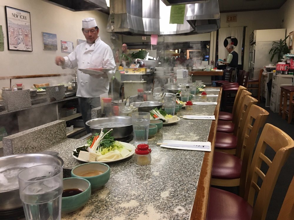Counter seating with a pot at every place and a cook behind the counter